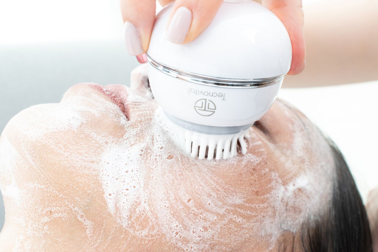 our-experience Woman's face being cleaned with an electric cleansing brush and foam.