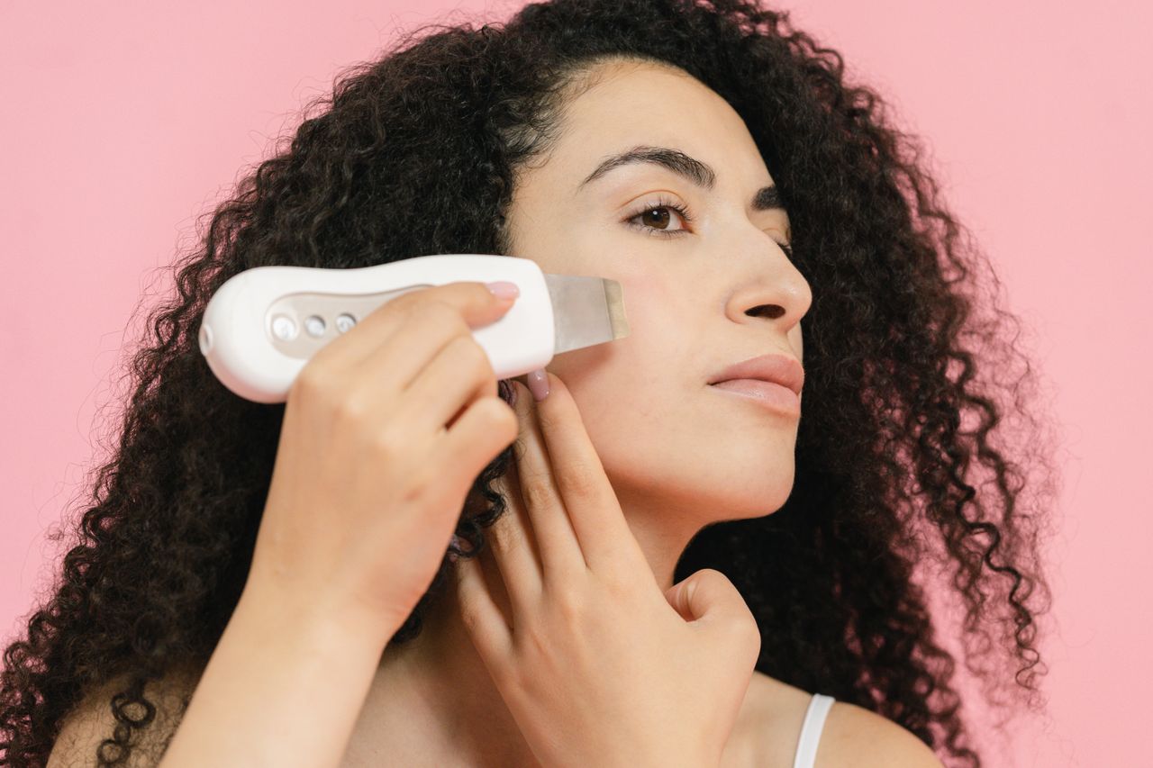 services-img Young woman with curly hair applying a cavitation peeling device, enhancing skincare routine.
